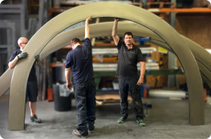 Fabrication team handling large curved aluminum profiles inside a manufacturing workshop, showcasing precision bending for architectural and industrial applications.